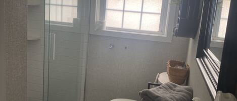 Kylpyhuone, jossa on lasiseinäinen suihkukaappi, wc, pesuallas ja ikkuna.