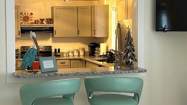 Una cocina con dos taburetes de color aguamarina, un reloj, armarios y un pequeño árbol de Navidad.