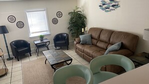 Una sala de estar con un sofá de cuero marrón, dos sillones negros, un sillón verde, una mesita y una planta en maceta.