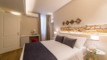 Habitación de hotel ordenada con cama, mesita de noche, lámpara y un adorno en la pared.
