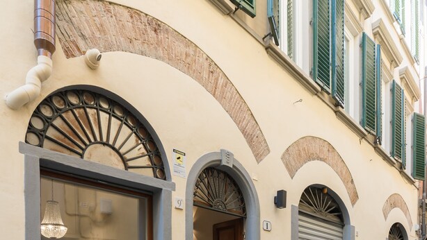 A building with arched doorways, a large window, and a stone-paved street. - Atelier Altafronte (Florence)