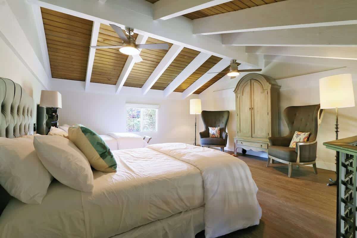 A bedroom with a large bed, wooden ceiling beams, a wardrobe, and two chairs.