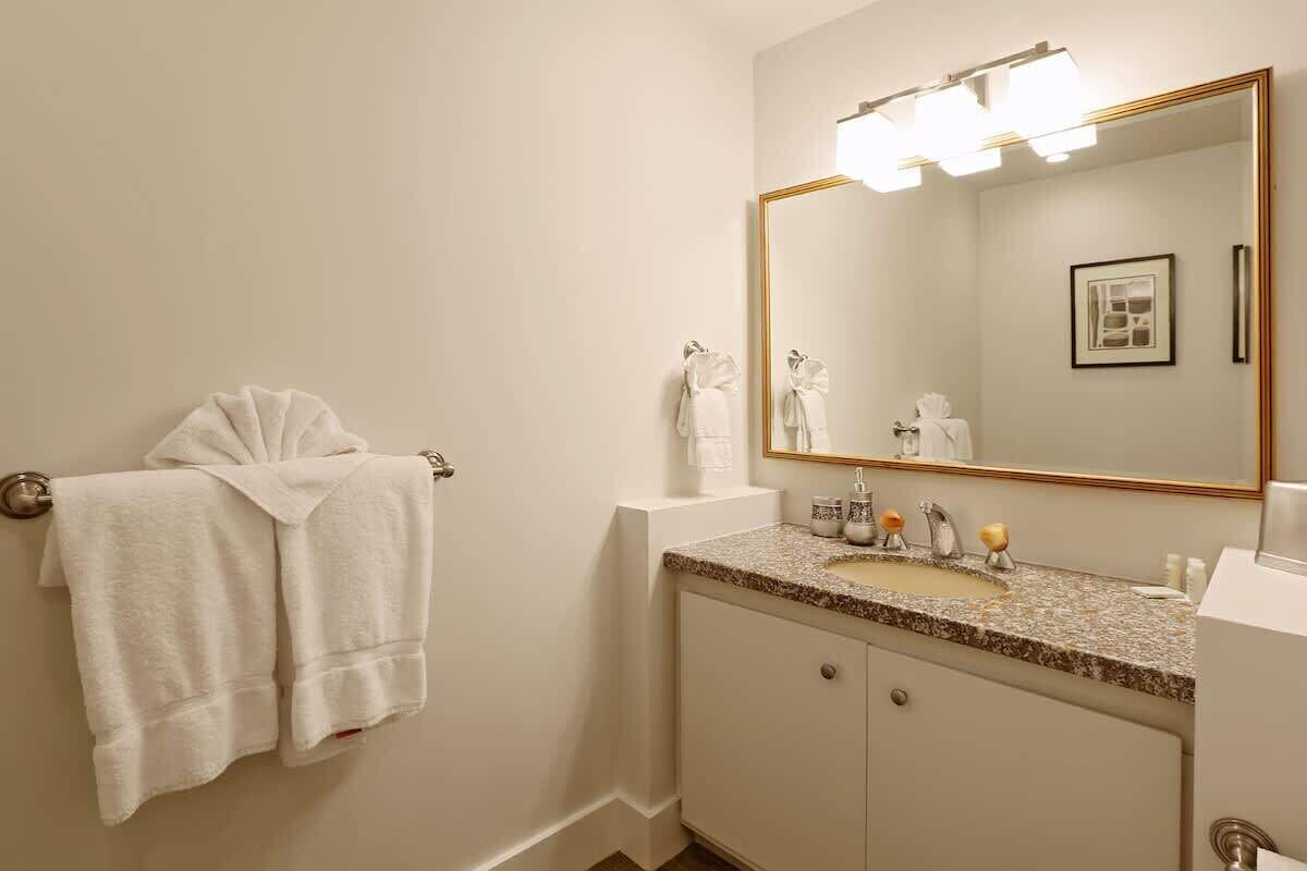 A bathroom with a large mirror, a sink with a granite countertop, and two towels hanging on a towel rack.