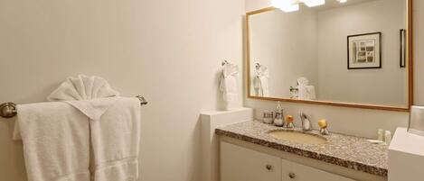 A bathroom with a large mirror, a sink with a granite countertop, and two towels hanging on a towel rack.
