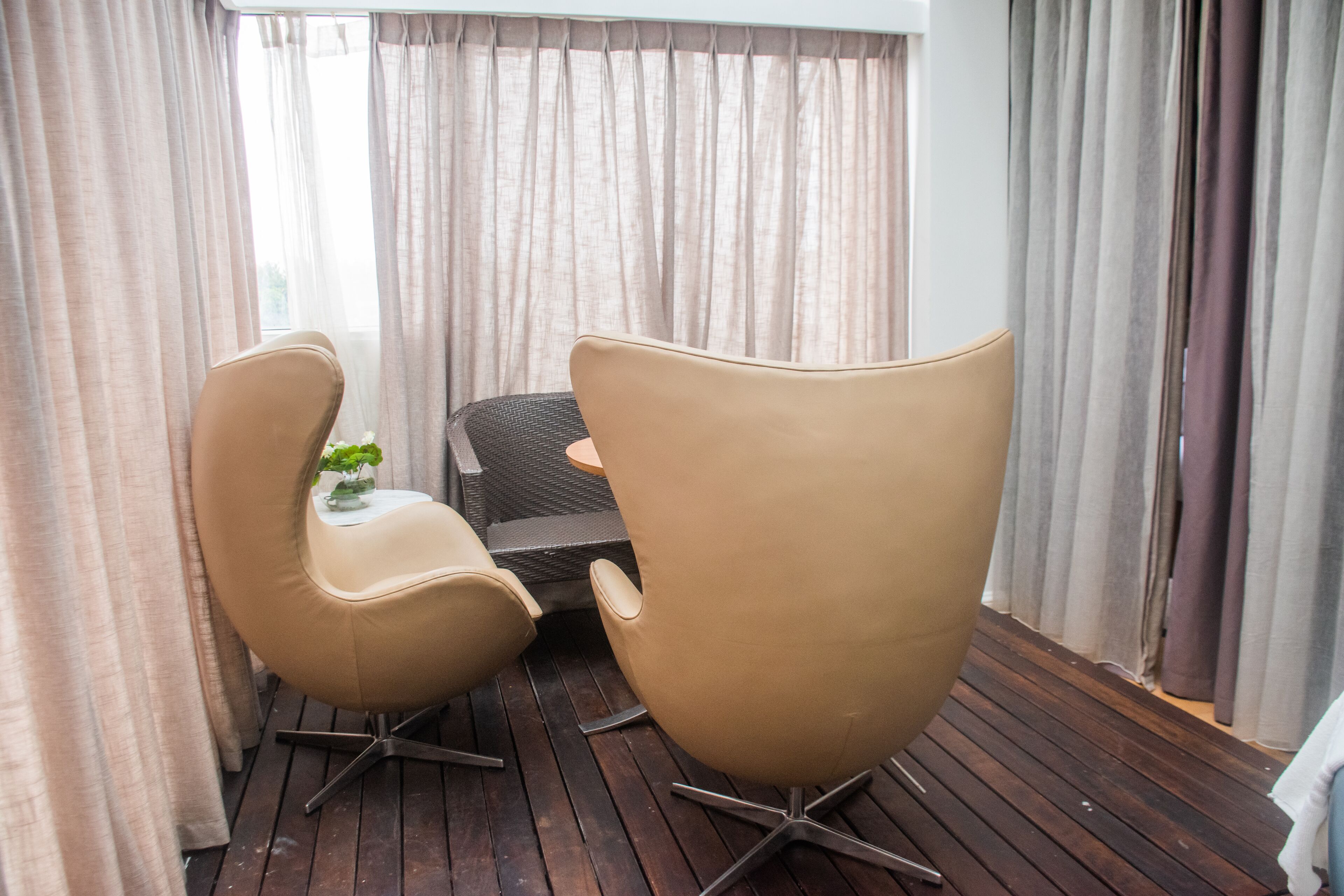 A room with two beige chairs, a small table with a plant, and a wicker chair.