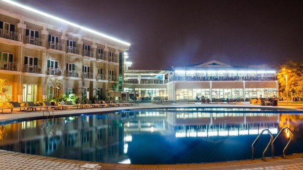 Vista nocturna de un hotel con piscina, varios balcones y fachada bien iluminada.