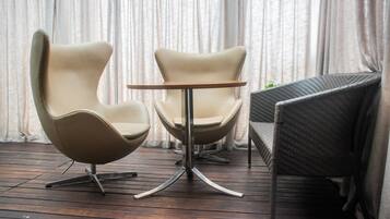 Two modern chairs with a round table in between, set on a wooden floor with a curtain backdrop.