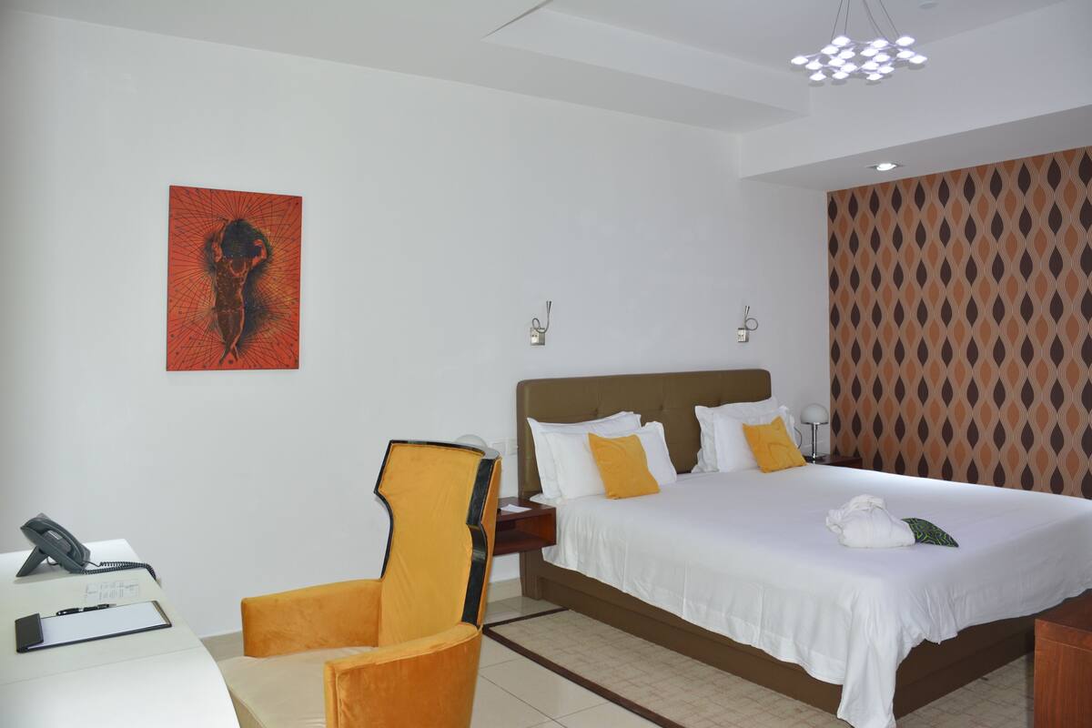 A hotel room with a bed, a desk, a chair, and a wall-mounted artwork.