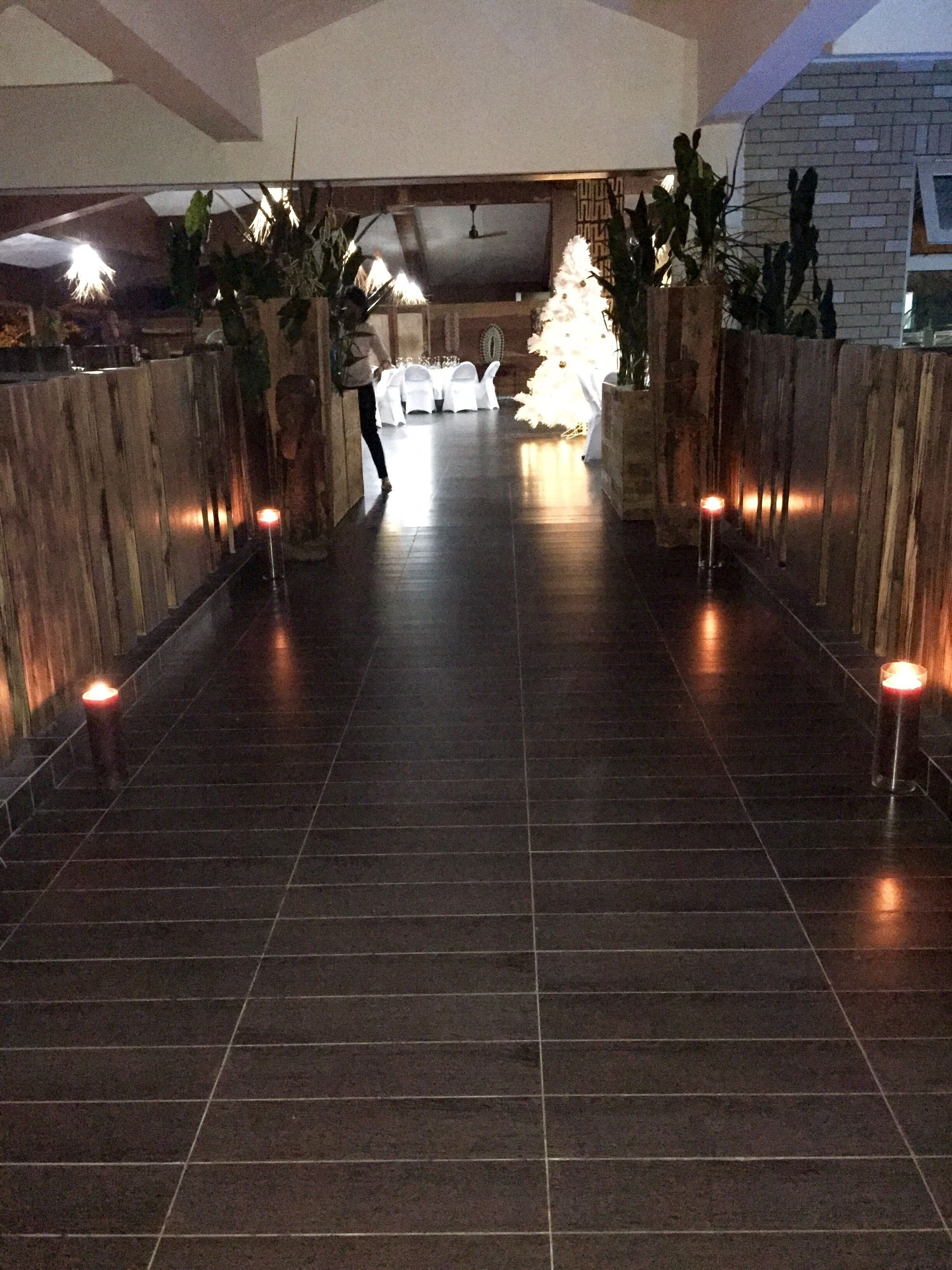 A corridor with a tiled floor leading to a seating area with white chairs and a table.