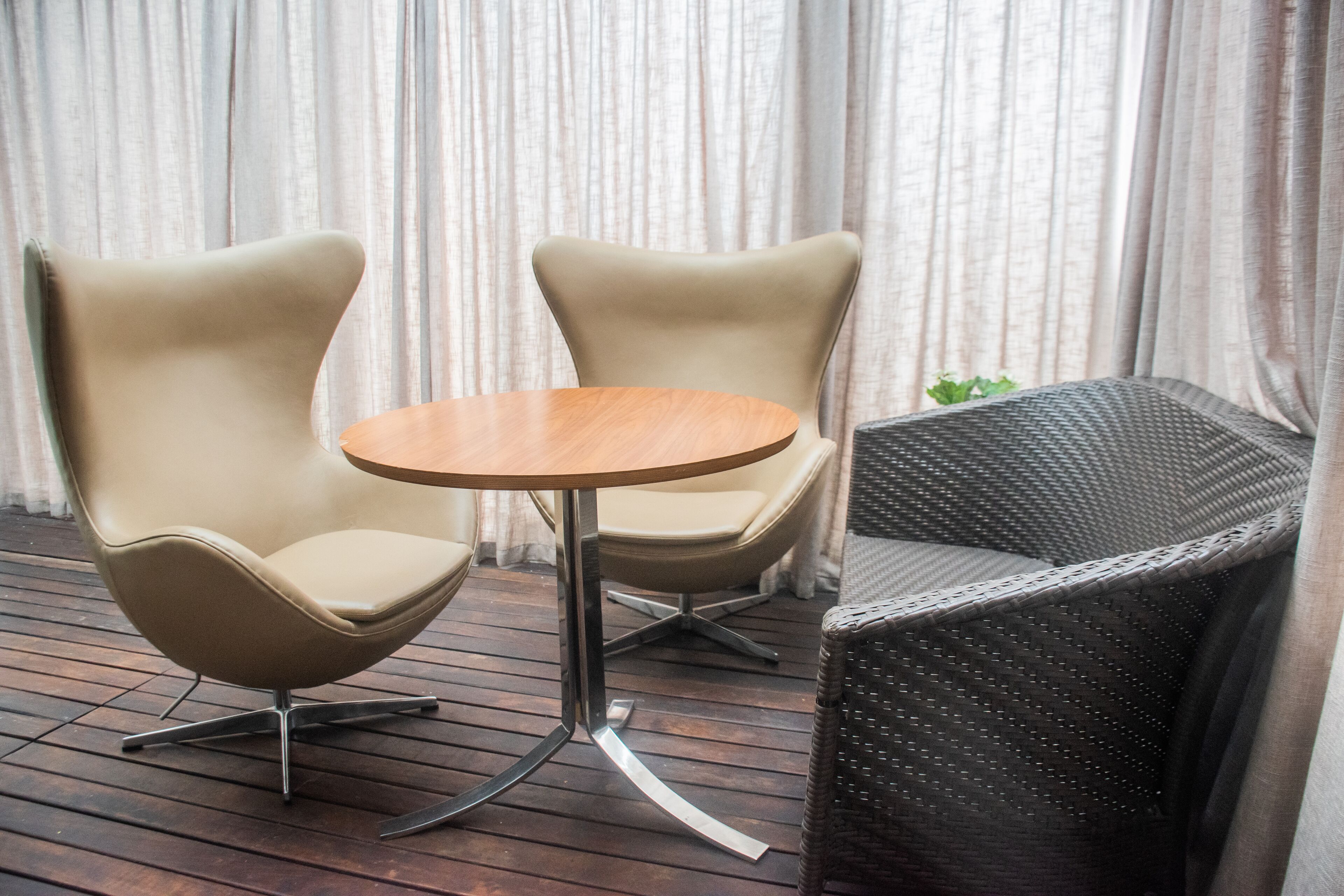 Une pièce moderne avec deux fauteuils à haut dossier et une table ronde, un canapé en osier et un fond constitué d’un rideau.