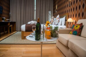 A hotel room with a bed, a sofa, a small table with drinks and a vase, and a wooden wall with a lattice design. - Pefaco Hotel Maya Maya (Brazzaville)