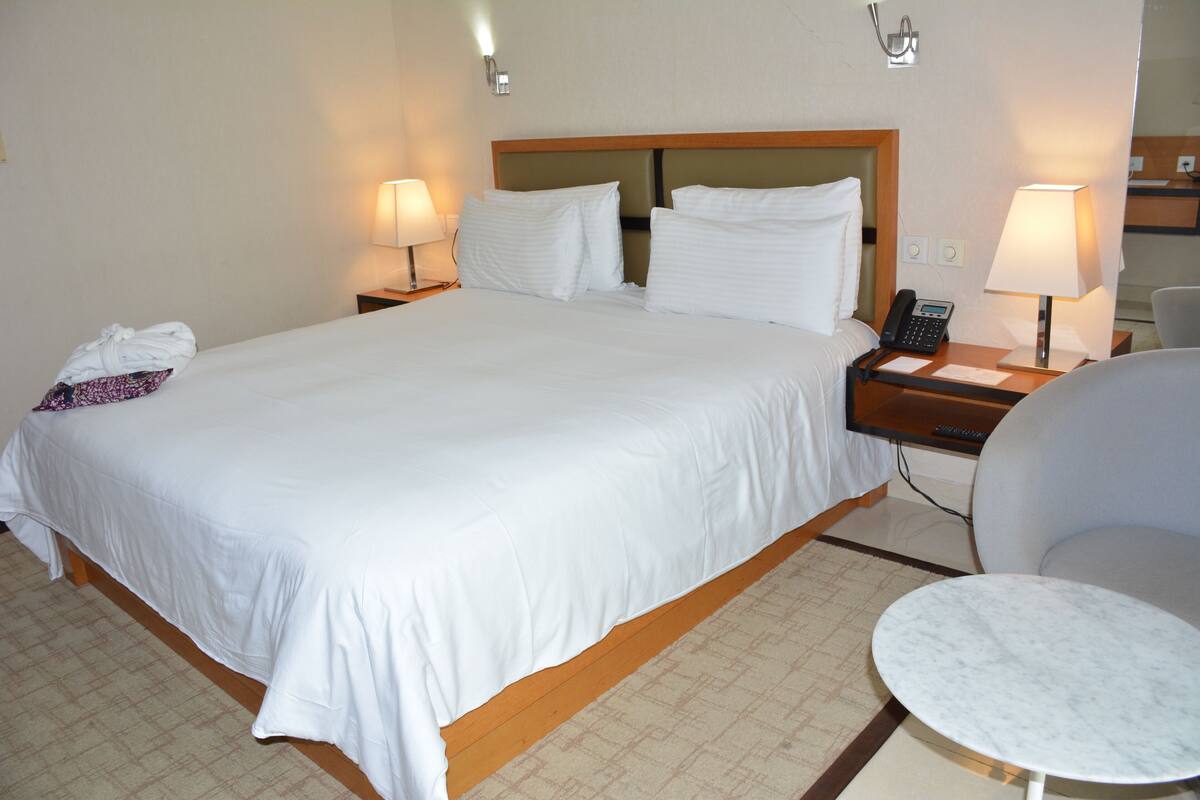 A hotel room with a large bed, two bedside tables with lamps, a chair, and a small table.
