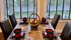 A dining table with a marble top, surrounded by black chairs, set with red bowls and a fruit basket in the center.