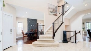 A spacious living area with a staircase, a dining area, and a large window.