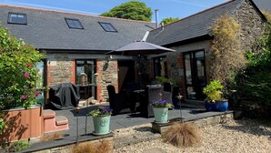 Una casa con fachada de piedra, techo de tejas y un patio cubierto con mobiliario exterior.