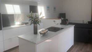 Una cocina moderna con armarios blancos, encimera de mármol, fregadero, cafetera y una planta en maceta.