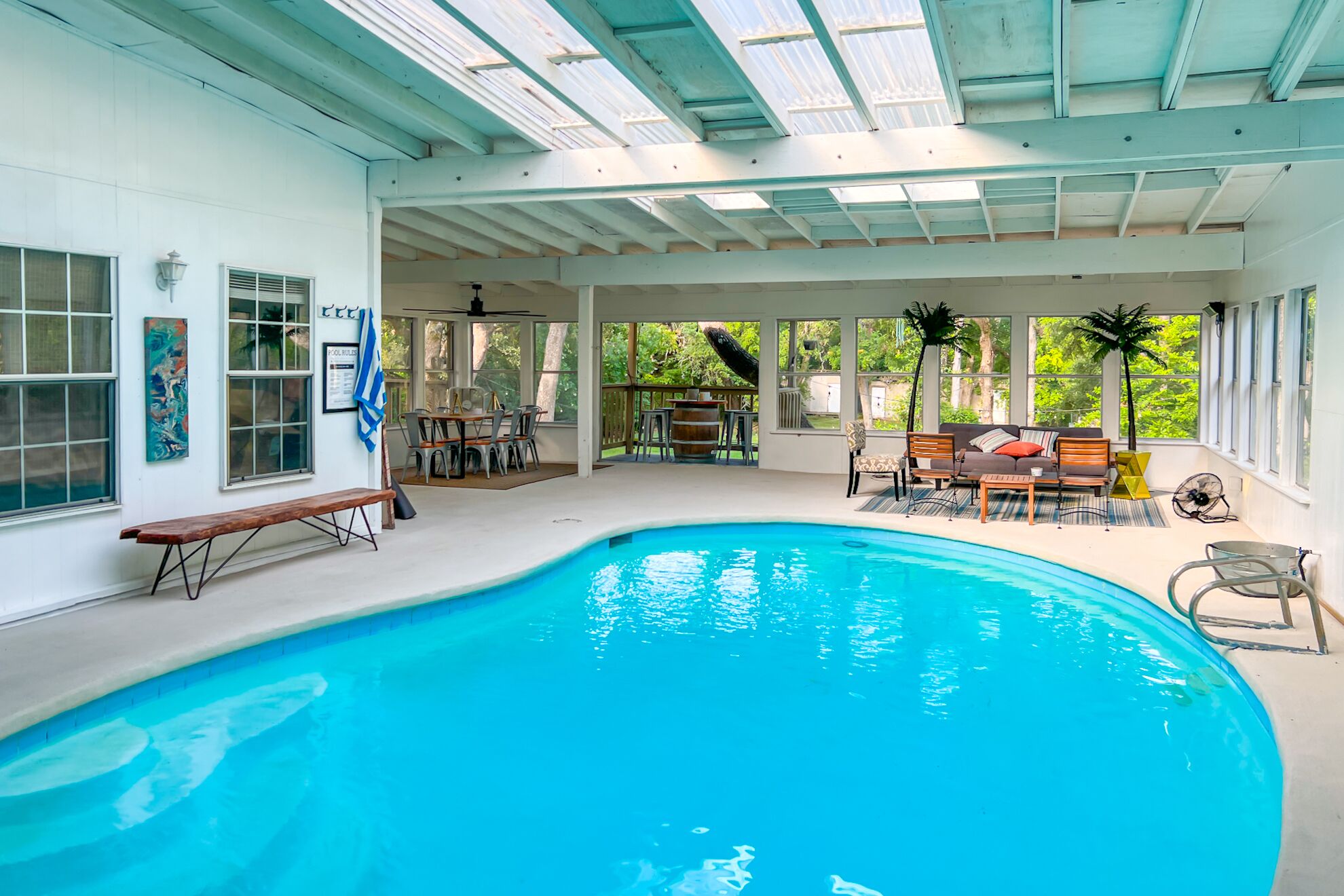 Piscina interior com teto panorâmico, rodeada por áreas de estar e vista para o verde.