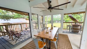 Une terrasse couverte avec une table et des chaises en bois, un ventilateur de plafond et une vue sur le jardin arrière.