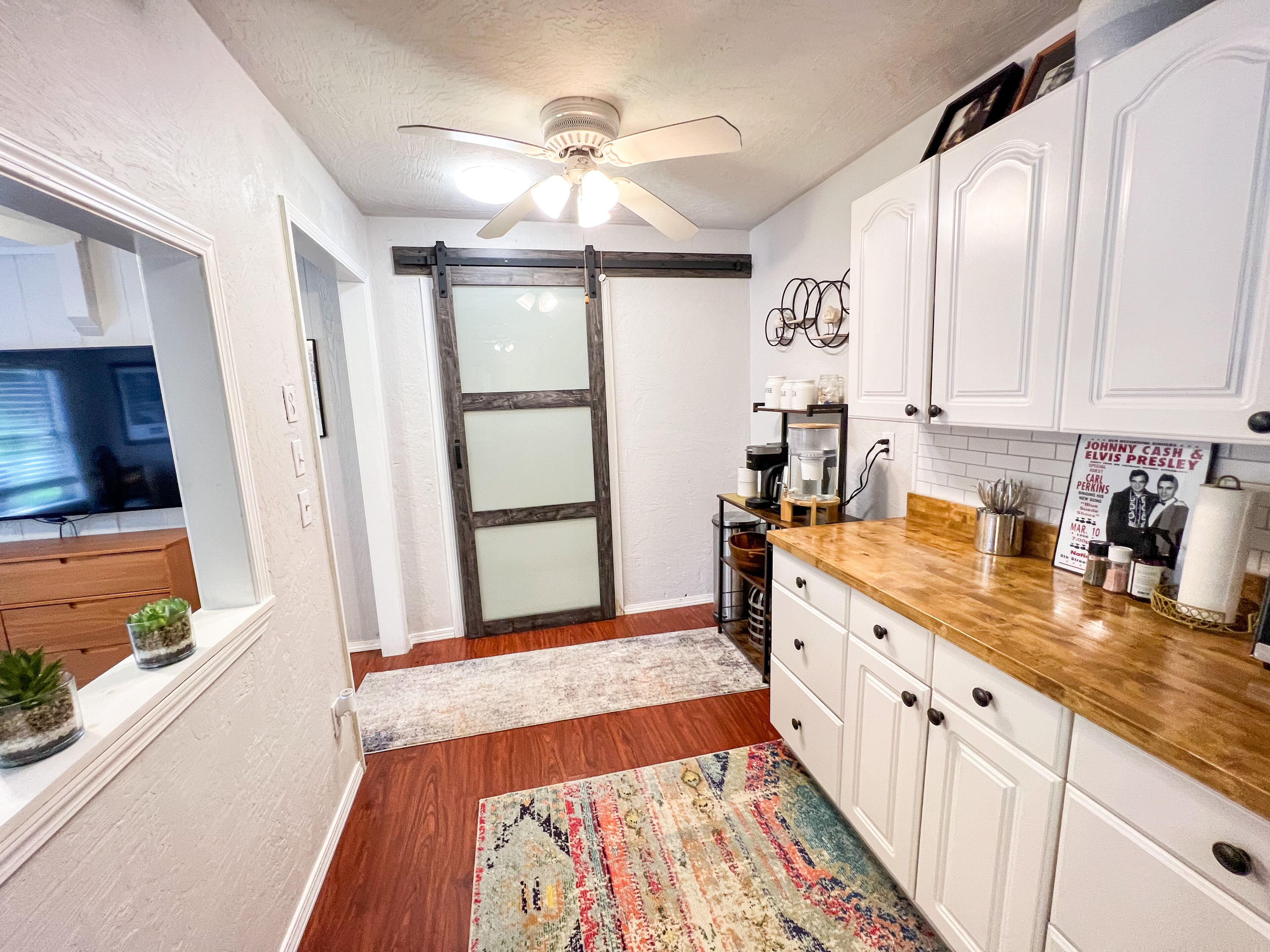 A kitchen with white cabinets, a wooden countertop, a ceiling fan, and a kitchen island with a coffee machine.