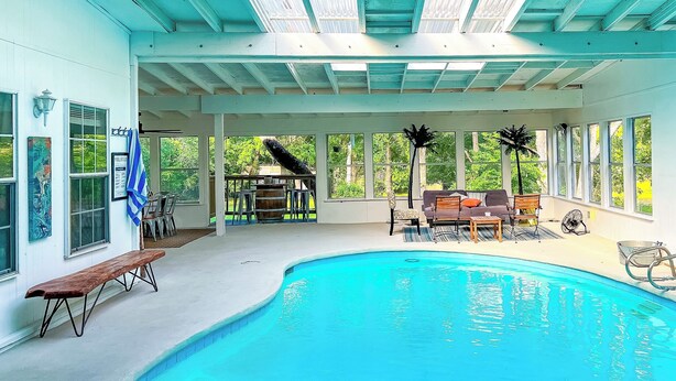 Une piscine extérieure couverte, dotée d’un banc et d’un espace détente, entourée de grandes fenêtres et d’une pergola.