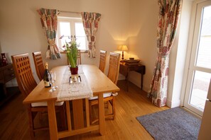 A dining room with a wooden table, chairs, a vase with flowers, a bottle, and a candle.