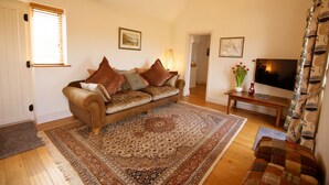 Ein gemütliches Wohnzimmer mit braunem Sofa, gemustertem Teppich, Holzboden und einem Fernseher auf einem Holztisch.