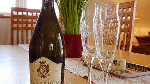 Eine Flasche Terra Bassa Prosecco auf einem Holztisch, zusammen mit zwei Weingläsern und einer Blumenvase.