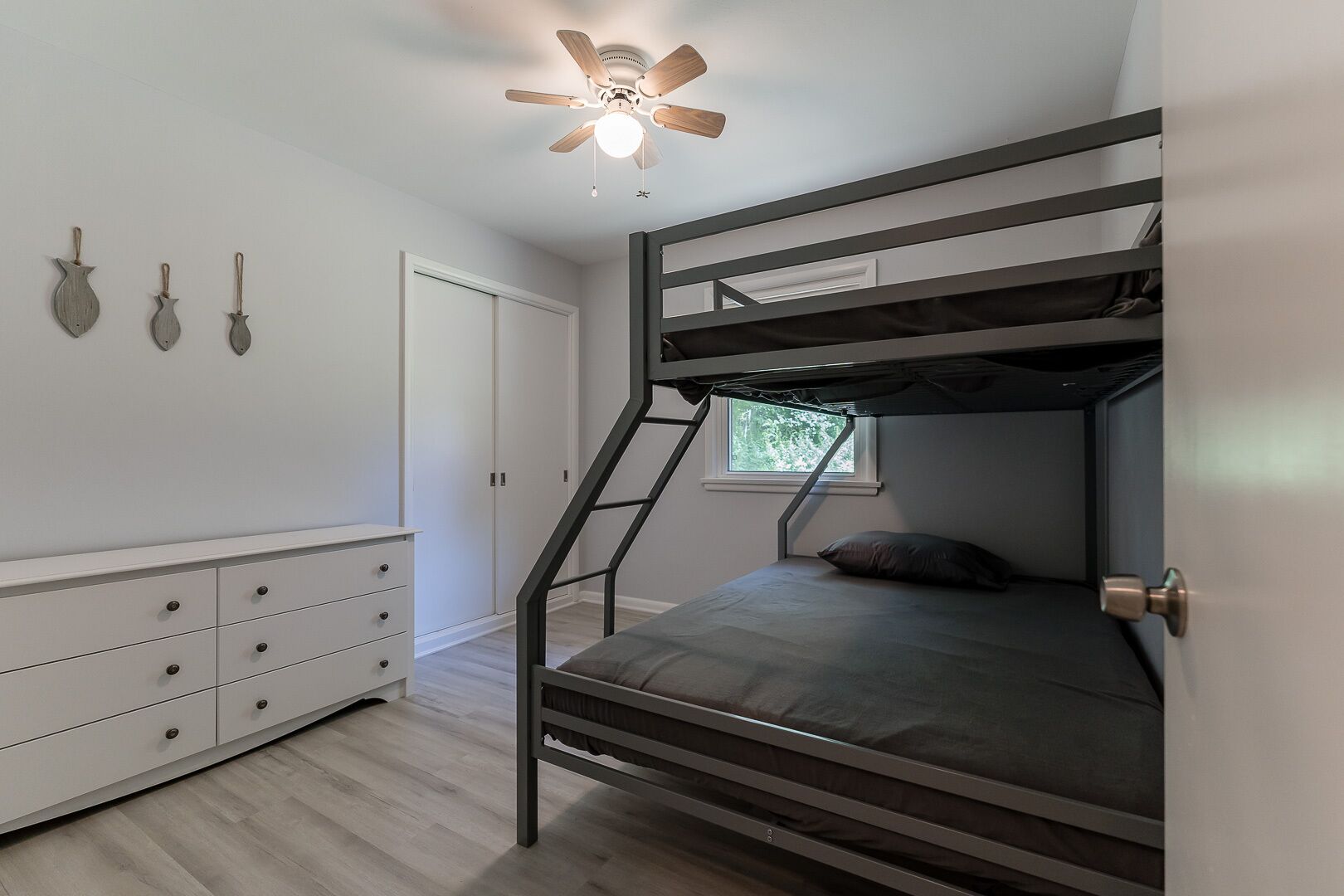 A bunk bed with a ladder, a white dresser, and a ceiling fan in a room with a window.