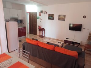 A living room with a sofa, a television, a small table, and a kitchen area with cabinets and a microwave. - Morada Sunset, Pool and bay view, Air Conditioned (Arona)