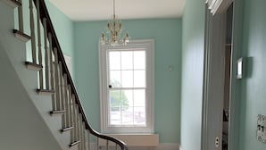 A hallway with a wooden staircase, a radiator, and a window with a view outside. - Captain Sweetser's Inn (Searsport)