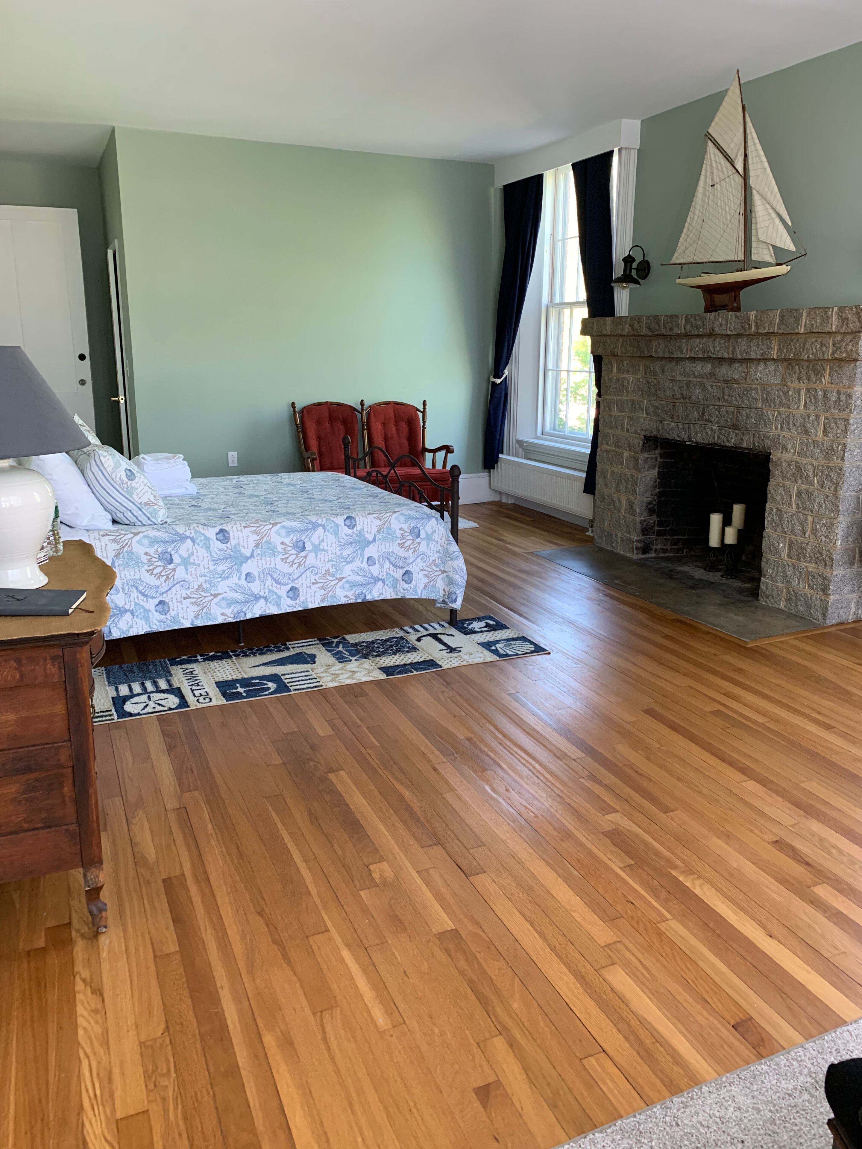 Una habitación con cama, chimenea, suelo de madera y ventana con cortinas.