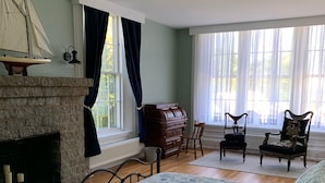 A bedroom with a bed, a fireplace, a dresser, two chairs, and a window with curtains. - Captain Sweetser's Inn (Searsport)