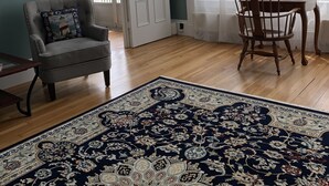 A room with a wooden floor, a large patterned rug, a dining table with chairs, a cushioned armchair, and a chandelier. - Captain Sweetser's Inn (Searsport)