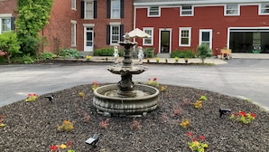 A brick building with a red exterior, a stone fountain in the center, and a well-maintained garden with various plants and flowers. - Captain Sweetser's Inn (Searsport)