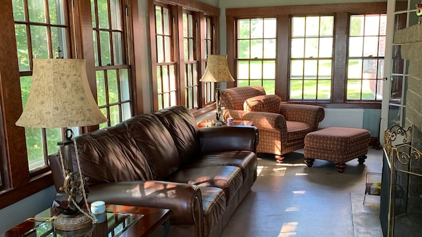 A spacious living room with a leather sofa, two armchairs, and a coffee table. Large windows allow natural light to fill the room. - Captain Sweetser's Inn (Searsport)