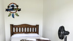 Ein ordentlich bezogenes Bett mit Holz-Kopfteil, Nachttisch und Standventilator.