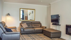 A modern living room with a sectional sofa, a single armchair, a flat-screen TV, and a large mirror on the wall. - 3 bedroom accommodation in Anstruther (Anstruther)