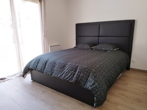 Une chambre à coucher moderne avec une tête de lit sombre, une couvre-lit à motifs géométriques et un parquet en bois clair.