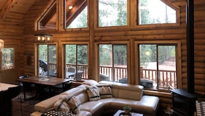 A log cabin interior with a dining area, a sofa, and large windows offering a view of the outdoors. - Beautiful & Brand New Cabin in Duck Creek  (Duck Creek Village)
