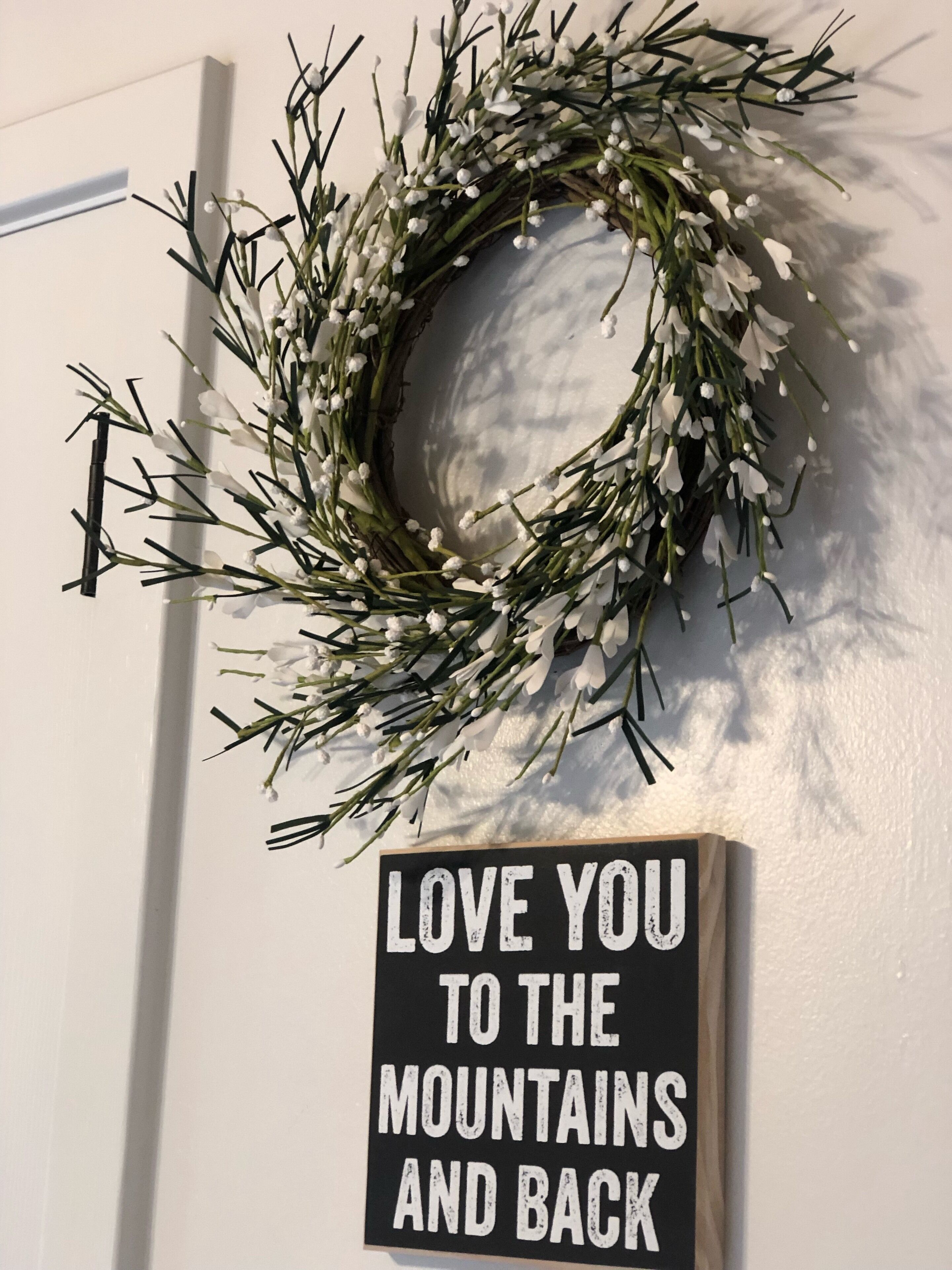 Un arreglo floral en una puerta con un letrero debajo que dice 'LOVE YOU TO THE MOUNTAINS AND BACK'.
