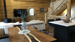 A wooden cabin interior with a dining table, chairs, a sofa, a TV, and a staircase. - Beautiful & Brand New Cabin in Duck Creek  (Duck Creek Village)