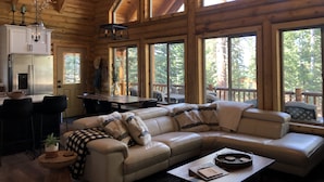 A log cabin interior with a dining area, a sofa, and large windows offering a view of the forest. - Beautiful & Brand New Cabin in Duck Creek  (Duck Creek Village)
