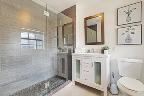 A modern bathroom with a glass shower enclosure, a vanity with frosted glass doors, a toilet, and framed artwork on the wall. - Family-Friendly Beach House, Steps to Beach (Fort Lauderdale)