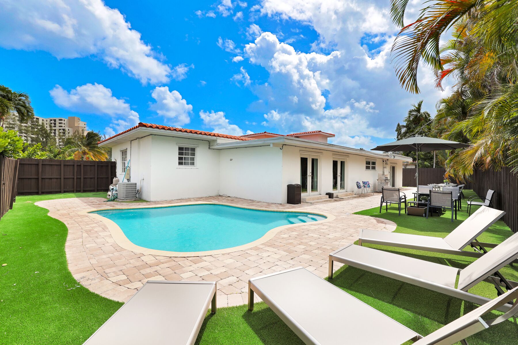 A backyard with a swimming pool, a patio with lounge chairs, and a house with a red-tiled roof.