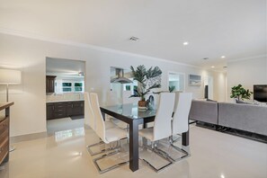A modern kitchen with dark cabinets, a glass dining table, and white chairs. - Family-Friendly Beach House, Steps to Beach (Fort Lauderdale)