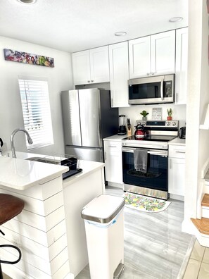 Fully equipped kitchen with stainless steel appliances, white countertop, sink, and trash can.