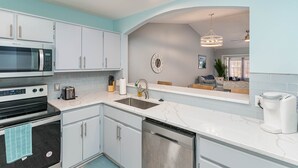 A modern kitchen with white cabinets, a stainless steel microwave, an oven, and a dishwasher. There is a sink with a faucet, a coffee maker, and a clock on the wall. - Perfect Private Navarre Beach Getaway! 4 minute from the beach! (Navarre)