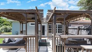 A covered outdoor patio with wooden benches and tables, a concrete floor, and a view of a house in the background. - Perfect Private Navarre Beach Getaway! 4 minute from the beach! (Navarre)