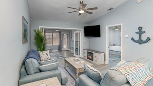 A spacious living room with a sofa, coffee table, and a fireplace. There is a ceiling fan, a television mounted on the wall, and a plant in the corner. - Perfect Private Navarre Beach Getaway! 4 minute from the beach! (Navarre)