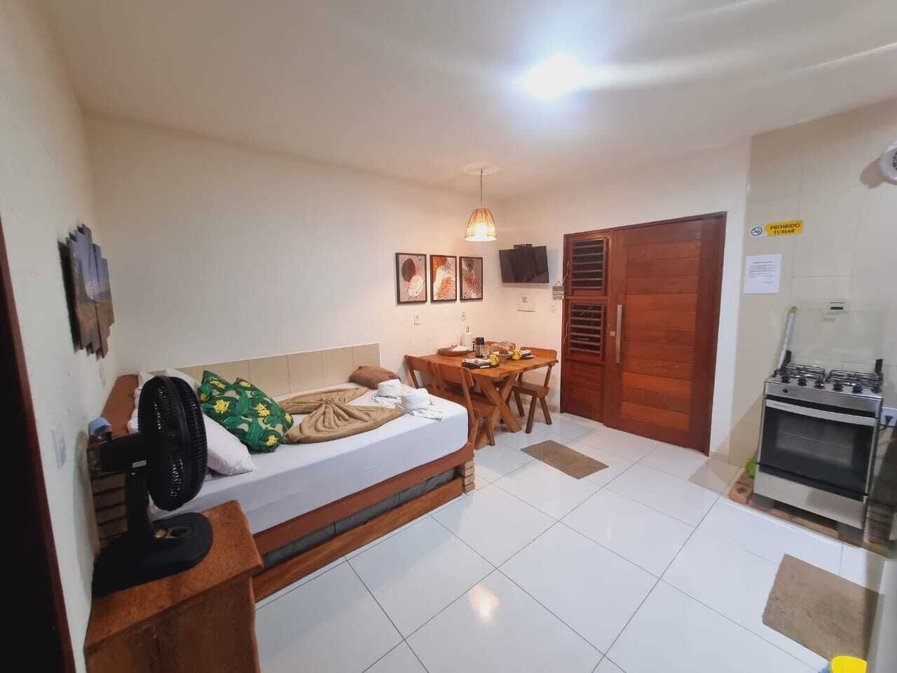 A compact room with a bed, a small table, a fan, and a kitchenette.